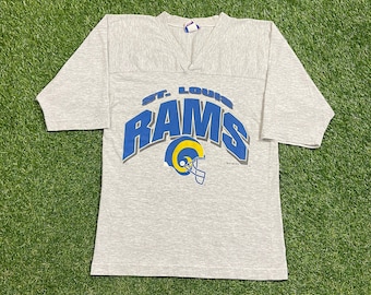 Op de afbeelding: Een grijs T-shirt met korte mouwen met een blauw en geel "St. Louis Rams" logo. Het logo toont een voetbalhelm met hoorns.
