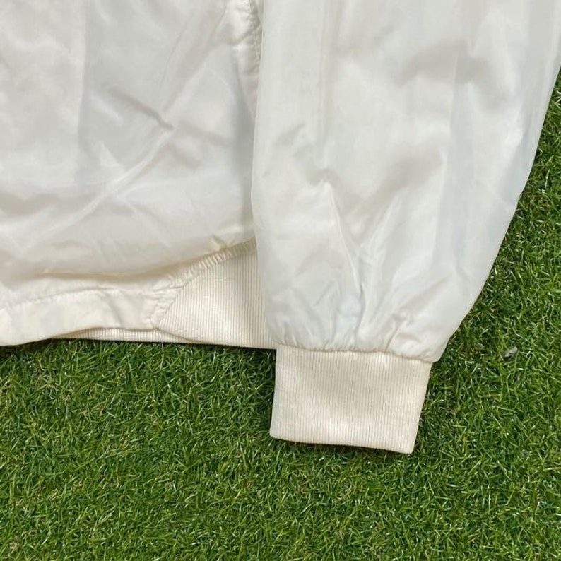 May include: A white lightweight jacket with a zipper closure and a ribbed knit collar, cuffs, and hem.