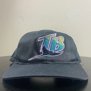 May include: Black baseball cap with a colorful embroidered logo of the letters "TB" with a stylized stingray underneath.