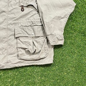 Pu&ograve; includere: Giacca color beige chiaro con pi&ugrave; tasche e chiusura a zip. La giacca ha una tasca con bottoni e una tasca sul petto con zip. La giacca &egrave; realizzata in un materiale leggero e presenta un dettaglio in pelle marrone sulla zip.