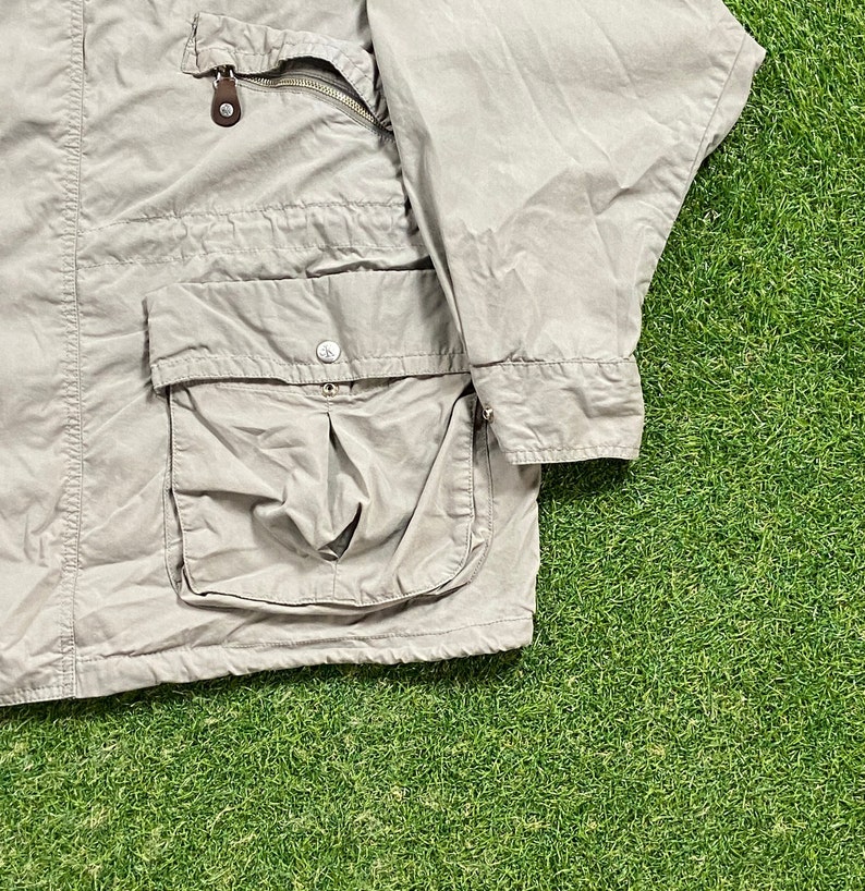 Pu&ograve; includere: Giacca color beige chiaro con pi&ugrave; tasche e chiusura a zip. La giacca ha una tasca con bottoni e una tasca sul petto con zip. La giacca &egrave; realizzata in un materiale leggero e presenta un dettaglio in pelle marrone sulla zip.
