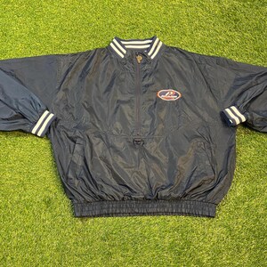 May include: Navy blue windbreaker jacket with a half-zip, stand-up collar, and elasticated cuffs. The jacket has white stripes on the collar and cuffs, and a logo on the chest. It's made of a lightweight, water-resistant material.