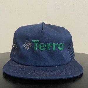 May include: A navy blue trucker hat with a green embroidered logo that says "Terra". The logo also includes a stylised grey mountain peak.
