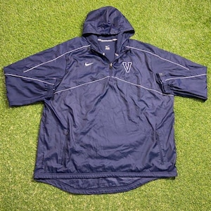 Puede incluir: Chaqueta con capucha azul marino con detalles blancos. Cuenta con cierre de cremallera, un logotipo blanco de Nike y un logotipo "V" blanco. La chaqueta tiene capucha con cordón y puños elásticos. Prenda deportiva.