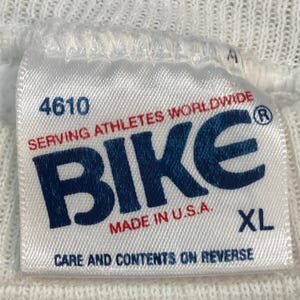 May include: White fabric tag with the word "BIKE" in navy blue, and the text "SERVING ATHLETES WORLDWIDE" in red. The tag also includes the text "MADE IN U.S.A." and "XL". The number "4610" is printed at the top of the tag.