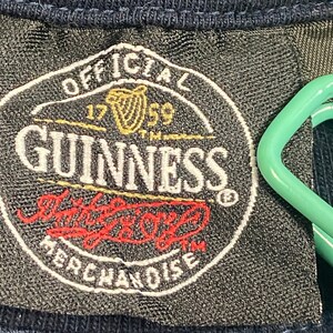 May include: Black and white label with the text "OFFICIAL 1759 GUINNESS" in a circle. The label also has a red and white logo with the text "The Original" and "MERCHANDISE" underneath.