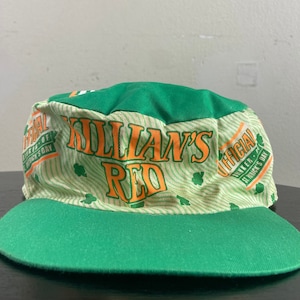May include: Green and white baseball cap with the words "Killian's Red" in orange and yellow. The cap has a green brim and a white crown with a green and white pattern. The text "Official Dinner - St. Patrick's Day" is printed on the side of the cap.