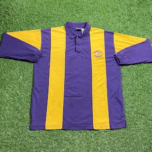 May include: A long-sleeved purple and gold striped polo shirt. The shirt features a purple collar and the words "Minnesota Vikings" embroidered on the chest. The shirt is made of a soft, comfortable material.