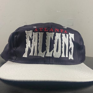 May include: A black and white baseball cap with the text "Atlanta Falcons" embroidered on the front in white with red accents.
