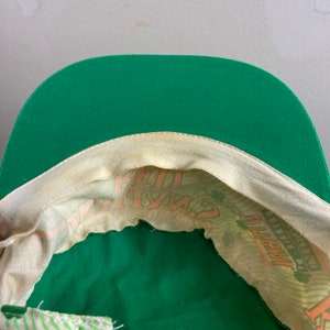 May include: Green baseball cap with a white and orange print inside. The print says "Lucky Charms" and has a shamrock.