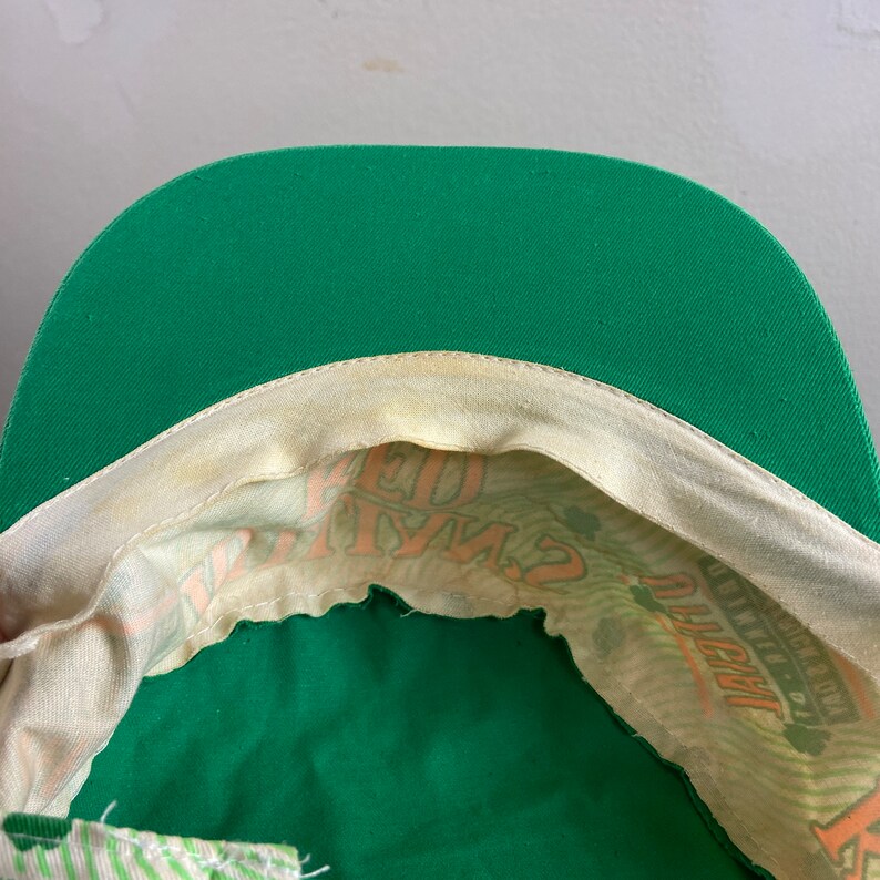 May include: Green baseball cap with a white and orange print inside. The print says "Lucky Charms" and has a shamrock.