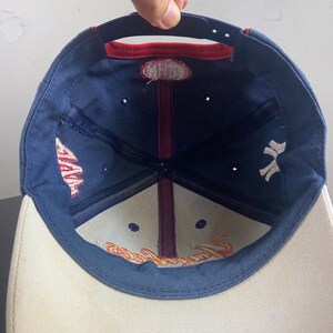 May include: A navy blue baseball cap with a white brim. The cap features the New York Yankees logo in white on the side and the word "Yankees" embroidered in gold on the inside. The cap has a red accent on the top.