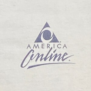 Może przedstawiać: Biały t-shirt z niebiesko-białym logo z napisem "America Online". Logo przedstawia stylizowany tr&oacute;jkąt z p&oacute;łksiężycem w środku.