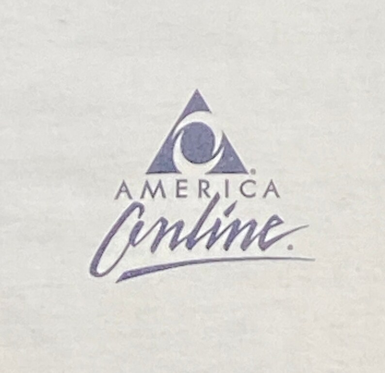 Może przedstawiać: Biały t-shirt z niebiesko-białym logo z napisem "America Online". Logo przedstawia stylizowany tr&oacute;jkąt z p&oacute;łksiężycem w środku.