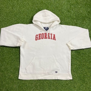 Puede incluir: Sudadera con capucha blanca con la palabra "GEORGIA" en letras rojas en la parte delantera.