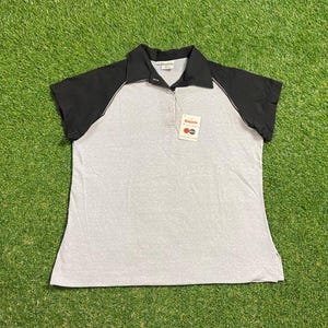 May include: A gray polo shirt with black sleeves and collar. The shirt has a white trim along the sleeves and a tag attached near the collar. The shirt is made of a soft material and has a classic design.