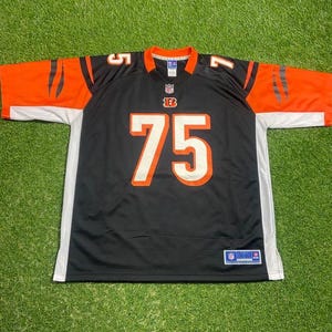 Può includere: Maglia da football nera e arancione con il numero 75 in bianco. La maglia ha dettagli bianchi e arancioni sulle maniche e sul colletto. Il logo NFL è visibile sulla maglia.