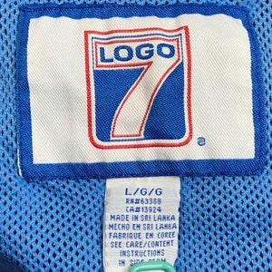 Peut inclure: Une &eacute;tiquette de v&ecirc;tement bleue et blanche avec le texte "LOGO 7" en rouge et blanc. L'&eacute;tiquette comprend &eacute;galement le texte "L/G/G", "RN#63388", "CA#13924", "MADE IN SRI LANKA", "MECHO EM SRI LANKA", "FABRIQUE EN COREE", "SEE CARE/CONTENT INSTRUCTIONS IN SIDE SEAM".