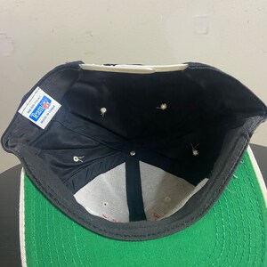 May include: Black and green baseball cap with a white brim and a white mesh lining. The cap has a black label on the inside that says "Team Up" and "One Size Fits All" with "Made in China" printed below.