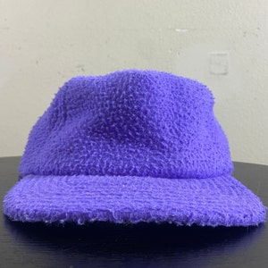 May include: A purple fuzzy bucket hat with a wide brim. The hat is made of a soft, textured fabric.