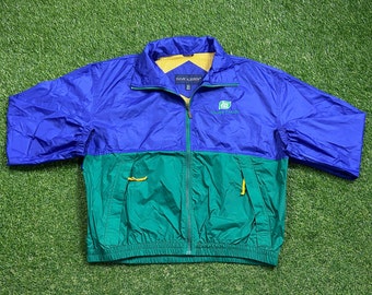 Könnte beinhalten: Eine blaue und grüne Windjacke mit Reißverschluss und einem Wrangler-Logo auf der Brust. Die Jacke hat einen grünen und gelben Kordelzug am unteren Rand.