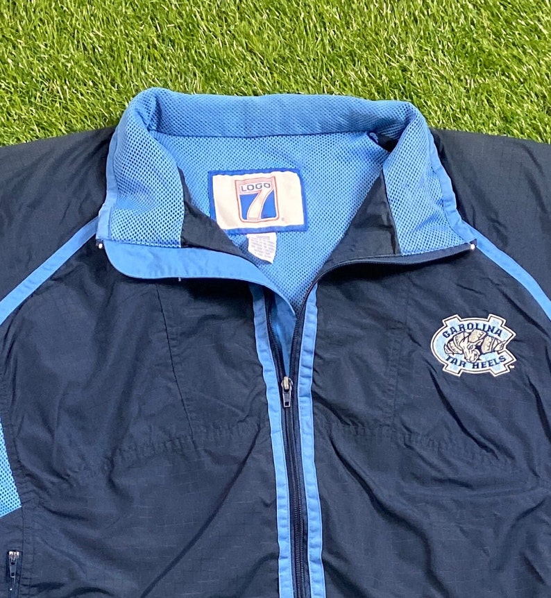 Peut inclure: Une veste coupe-vent bleu marine avec des accents bleu clair et un logo Carolina Tar Heels sur le c&ocirc;t&eacute; droit. La veste a une fermeture &eacute;clair et une doublure en mesh.