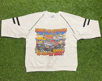 May include: White long-sleeved sweatshirt with black racing stripes on the sleeves. The front of the sweatshirt features a colourful graphic of race cars with the text "World of Outlaws Greatest Show on Dirt".