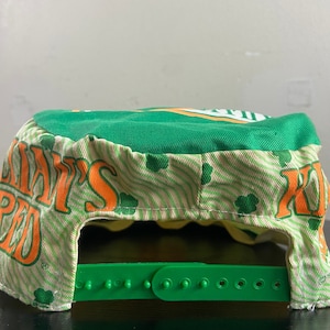 May include: Green and white baseball cap with an orange and white logo that says "Shamrock's Pub". The cap has a green adjustable strap.
