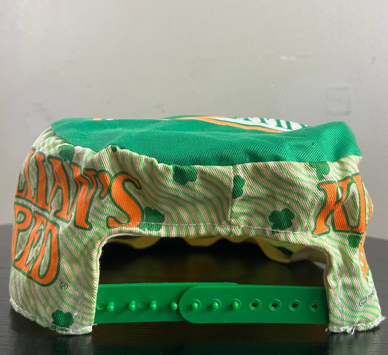 May include: Green and white baseball cap with an orange and white logo that says "Shamrock's Pub". The cap has a green adjustable strap.