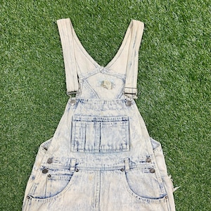 May include: Light blue denim overalls with a faded, distressed look. The overalls have adjustable straps and a large pocket on the front.