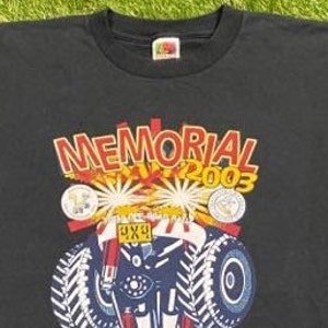 Może przedstawiać: Czarny T-shirt z grafiką przedstawiającą monster trucka z napisem "MEMORIAL DAY 2003" i "4X4" na samochodzie.