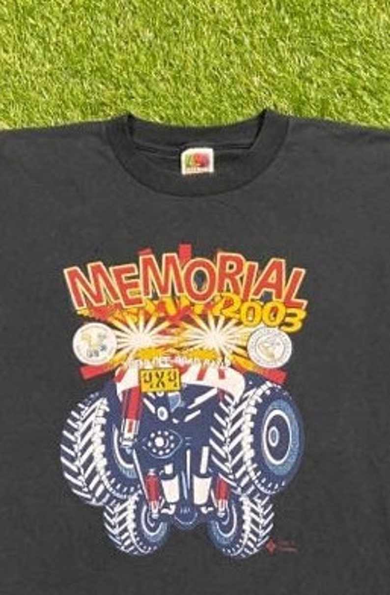 Może przedstawiać: Czarny T-shirt z grafiką przedstawiającą monster trucka z napisem "MEMORIAL DAY 2003" i "4X4" na samochodzie.