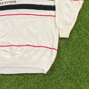 May include: White striped sweater with a black and red stripe pattern. The sweater has the word "GUINNESS" printed on the top.