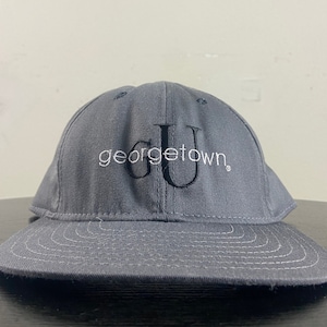 Puede incluir: Gorra de béisbol gris con un logotipo bordado en negro de la Universidad de Georgetown.