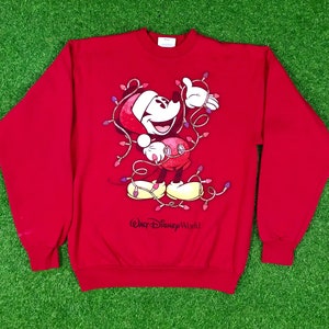 Könnte beinhalten: Roter Weihnachtspullover mit Mickey Mouse, der einen Weihnachtsmann-Hut trägt und in Weihnachtslichter verwickelt ist. Der Pullover hat den Text "Walt Disney World" unten aufgedruckt.