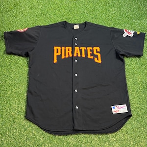 May include: Black baseball jersey with the word "PIRATES" in orange lettering across the chest. The jersey has a button-up front and patches on the sleeves. A "Rawlings" tag is visible.