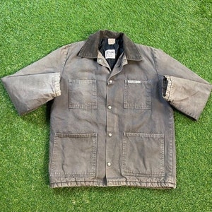 May include: A dark gray work jacket with a corduroy collar and multiple pockets. The jacket has a button closure and a brand label that reads "Prince".