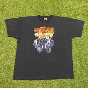 Może przedstawiać: Czarny T-shirt z grafiką przedstawiającą monster trucka z nadrukiem "MEMORIAL DAY 2003" i "4X4".