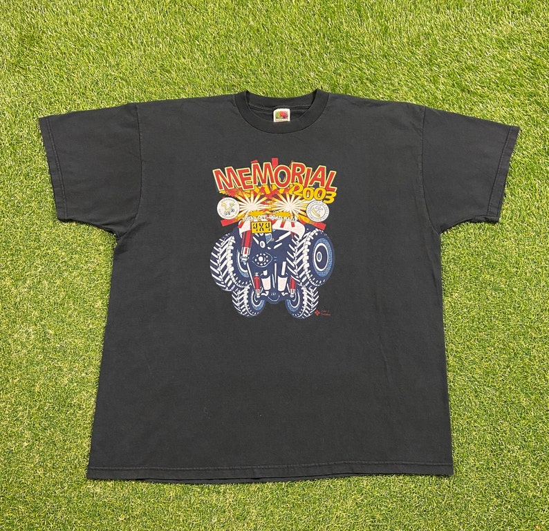 Może przedstawiać: Czarny T-shirt z grafiką przedstawiającą monster trucka z nadrukiem "MEMORIAL DAY 2003" i "4X4".