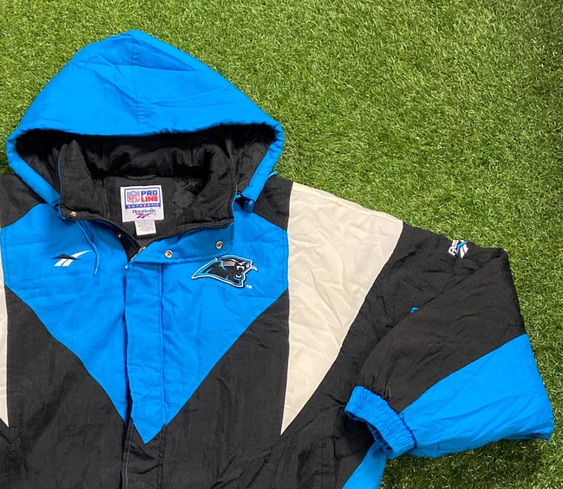 Peut inclure: Veste &agrave; capuche noire, blanche et bleu Carolina. La veste pr&eacute;sente le logo des Panthers de la Caroline sur la poitrine et les logos Pro Line et Reebok. La veste a une fermeture &eacute;clair compl&egrave;te et des poignets &eacute;lastiques.
