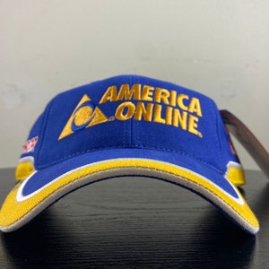 May include: A blue baseball cap with a yellow brim and a white stripe. The front of the cap has a gold embroidered logo that says "America Online" with a stylized "A" in a triangle.
