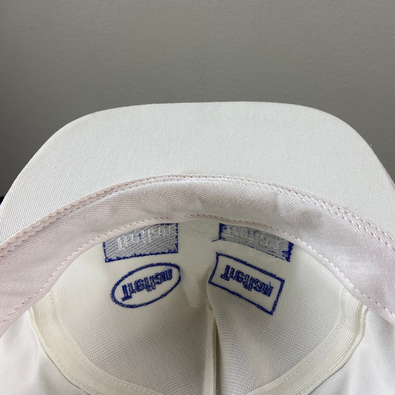 May include: White baseball cap with a blue embroidered logo that reads "Resist" on the inside of the cap.