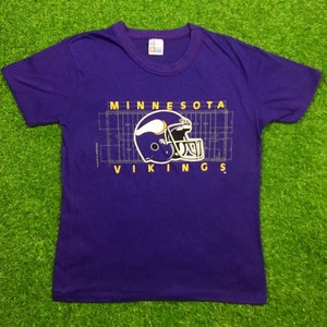May include: Purple t-shirt with a Minnesota Vikings logo and a football field graphic. The logo features a purple helmet with a yellow horn and the text "MINNESOTA VIKINGS".