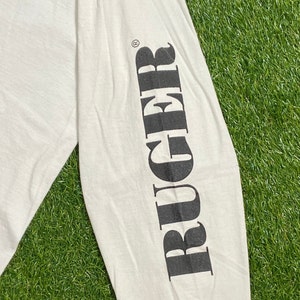 K&ouml;nnte beinhalten: Wei&szlig;es Langarm-T-Shirt mit dem Wort "RUGGER" in Schwarz auf dem linken &Auml;rmel.