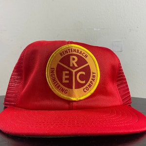 May include: Red and yellow trucker hat with a logo that says "Rentenbach Engineering Company" and has the letters "R E C" inside a circle.