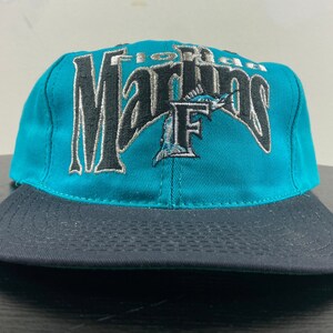 May include: Teal and black baseball cap with the embroidered text "Florida Marlins" and a stylized "F" with a marlin fish.