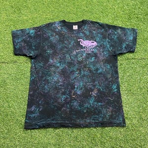 May include: A short-sleeve t-shirt with a black, teal, and purple tie-dye pattern. The chest features a light purple graphic of an elephant above the text LOS ANGELES ZOO. The shirt has a crew neckline and a standard fit with a straight hemline.