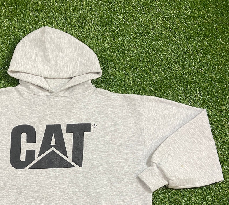 May include: A gray hooded sweatshirt with a black CAT logo on the front. The logo is a stylized letter C with a triangle inside.