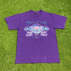 May include: Purple short-sleeved t-shirt with a graphic of a mountain range and the text "MONTANA THE LAST BEST PLACE".