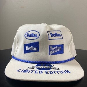 May include: White baseball cap with blue embroidered logos of the brand "Treflan" and the text "Anniversary Limited Edition".